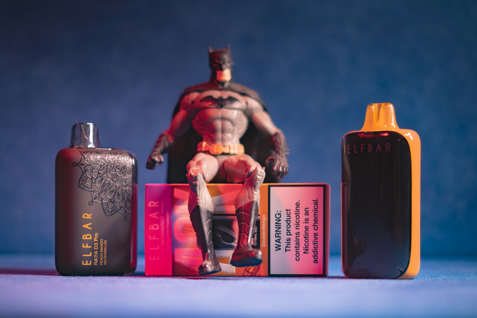 Batman figure sitting on vape packaging with devices
